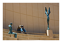 photo of a man with head down on stairs between sculptures